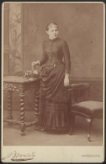 Młoda kobieta stojąca przy stole [fotografia]