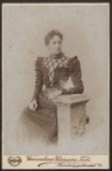 Kobieta siedząca przy postumencie [fotografia]