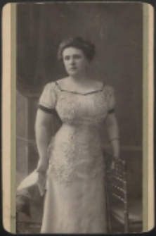 Kobieta stojąca przy krześle[fotografia]