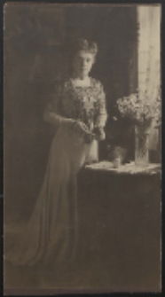 Kobieta stojąca przy stoliku z bukietem kwiatów [fotografia]