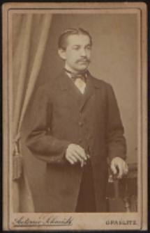 Mężczyzna stojący przy fotelu [fotografia]