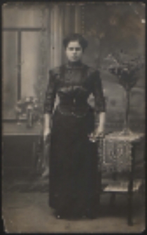 Młoda kobieta stojąca przy stoliku [fotografia]