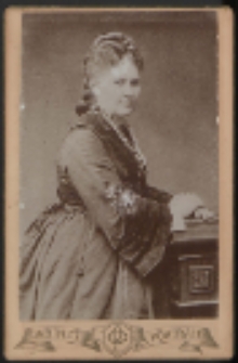 Kobieta stojąca przy stoliku [fotografia]