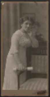 Młoda kobieta stojąca przy fotelu [fotografia]