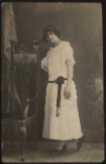 Młoda kobieta stojąca przy krześle [fotografia]